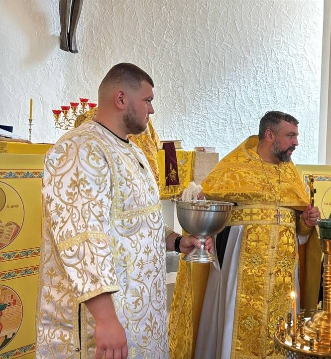 Двоє священників у золотих ризах біля престолу, у руках срібна чаша, поруч свічки