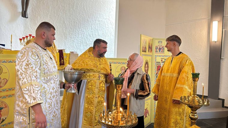 Духовенство в золотих і білих ризах біля престолу, посудина зі свяченою водою й свічники