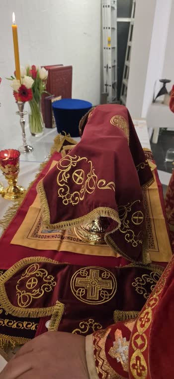 Престол під червоними покровами з золотим шитвом, свічка й квіти