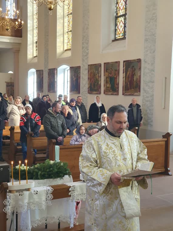 Священник читає посеред храму, громада слухає, попереду хвоя зі свічками