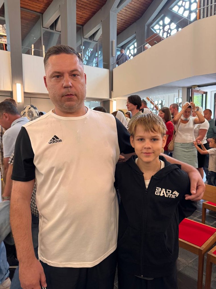 Чоловік обіймає хлопця за плече, позаду повна каплиця