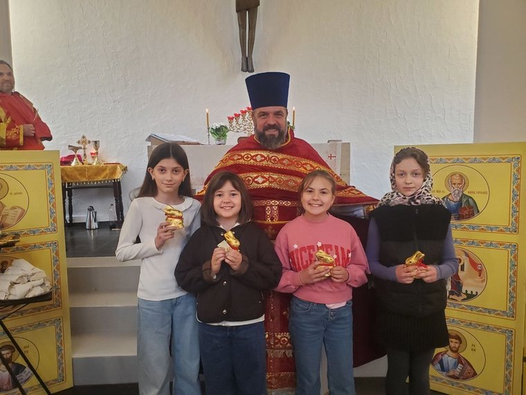 Der Priester in roten Gewändern und vier Kinder mit Schokoladenhasen am Altar