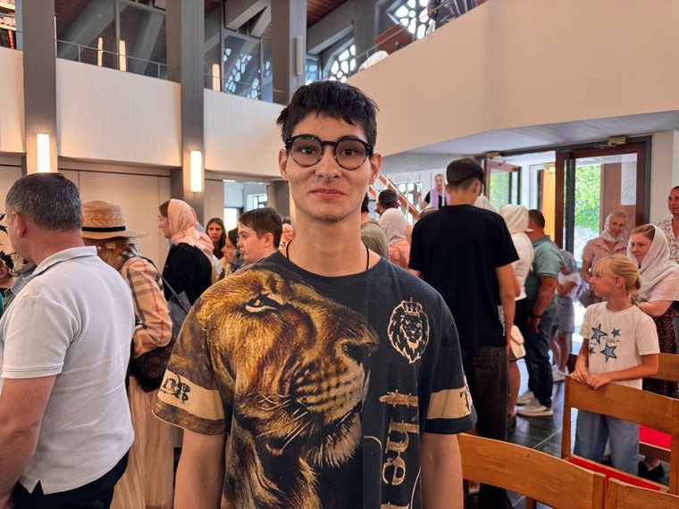 Ein junger Mann mit Brille lächelt mitten in der vollen Kapelle